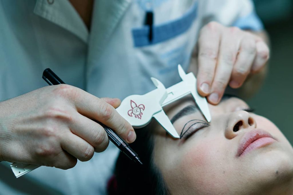 Woman laying in front of a plastic surgeon having her eye measured for a procedure